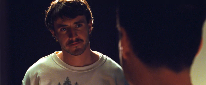 Intense scene from All of Us Are Strangers movie featuring a close-up of a male actor with a mustache in a serious confrontation.