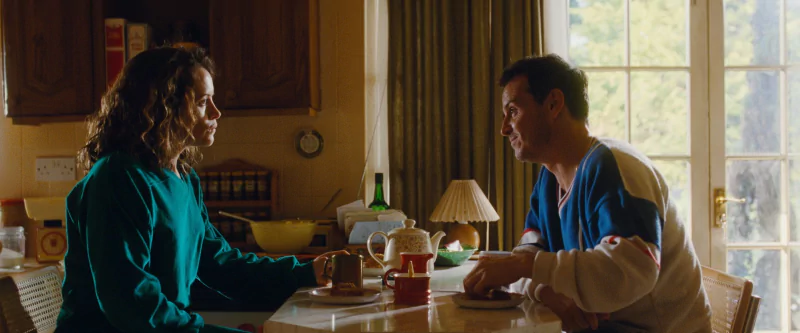 Intense conversation scene from All of Us Strangers movie with two characters sitting at a kitchen table.