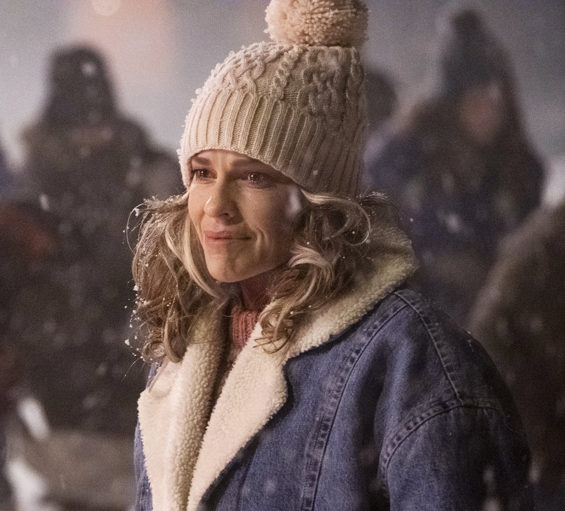 Woman in a winter hat and denim jacket smiling in a snowy scene from the movie Ordinary Angels.