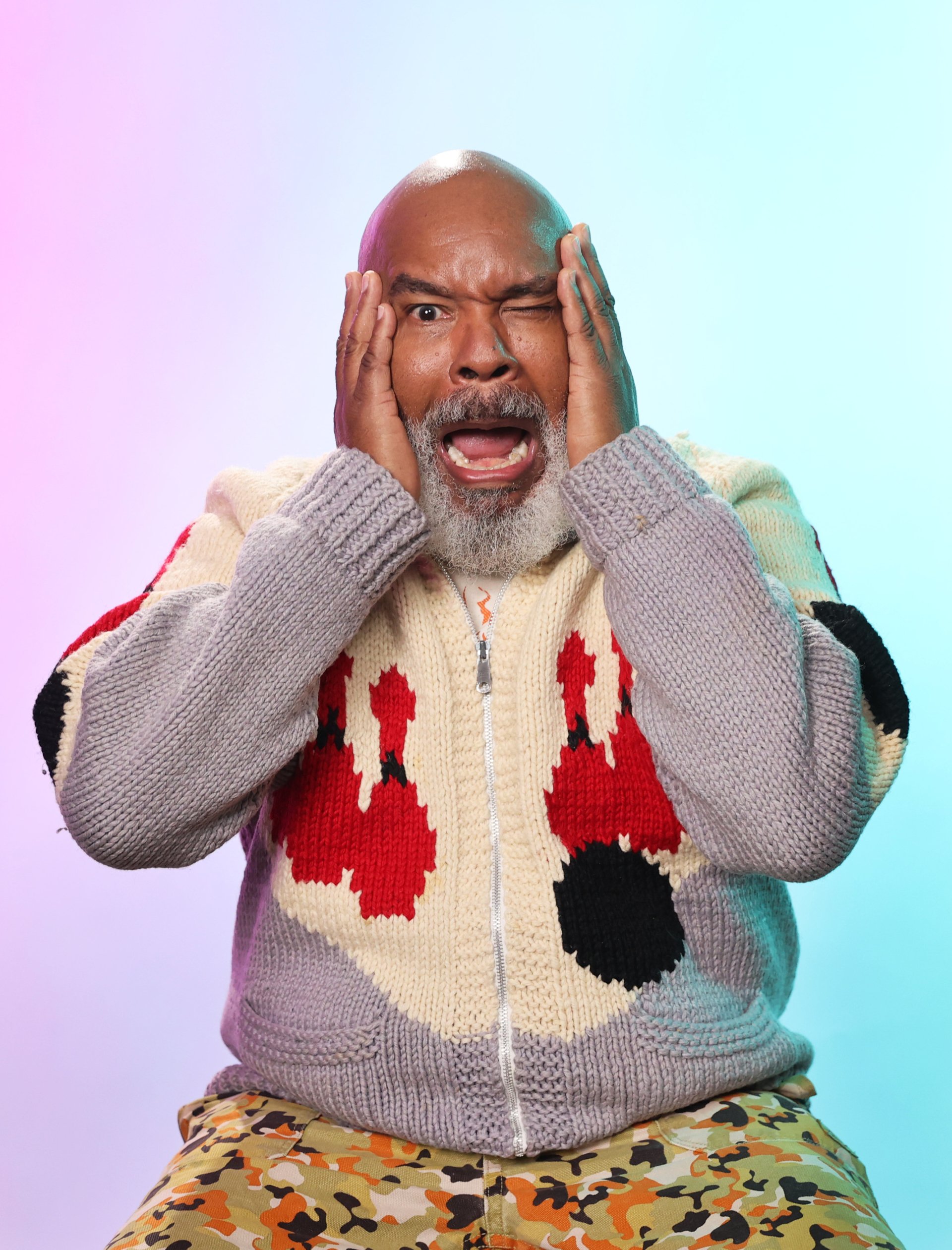 Man in colorful sweater looking shocked with hands on face against gradient background, promoting The American Society of Magical Negroes TV show.