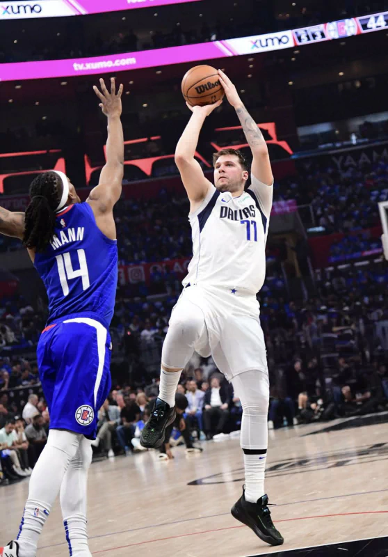 Luka Dončić of the Dallas Mavericks shoots a basketball during an NBA game, defended by an opponent wearing number 14.
