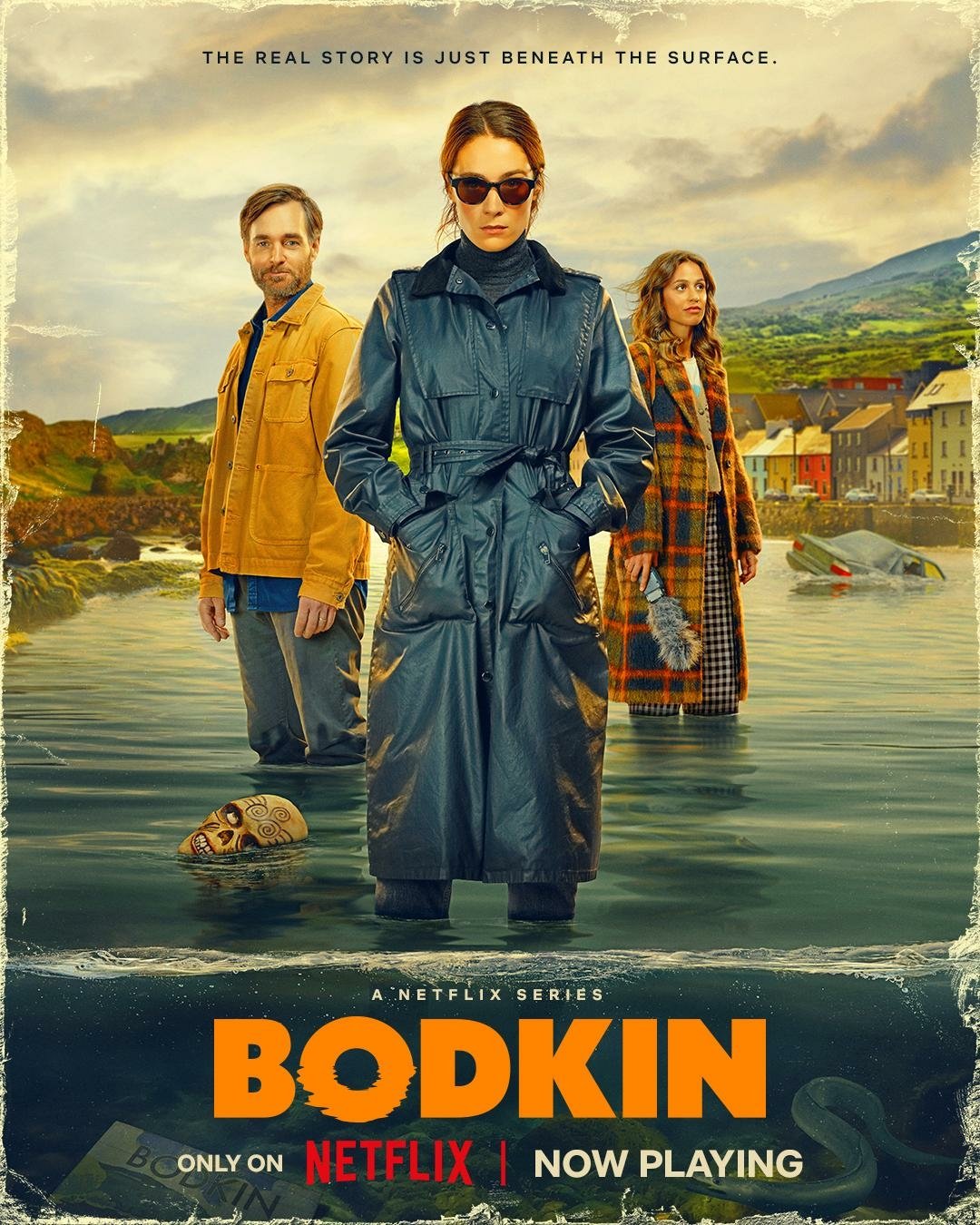 Poster for the TV show Bodkin featuring three characters standing in water with a coastal village backdrop, now streaming on Netflix.