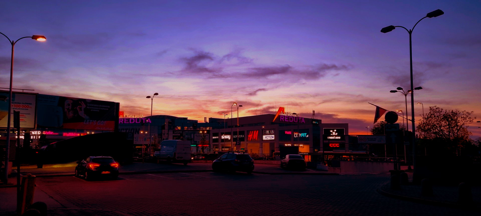 City shopping area under an evening sky with colorful clouds and illuminated storefronts along the street.
