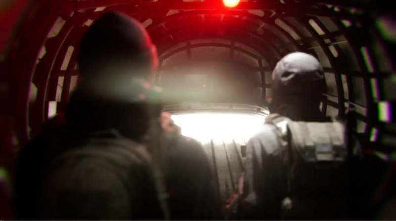 A video game scene depicting a bodycam view of two characters dressed in tactical gear navigating through a dimly lit, tunnel-like structure.