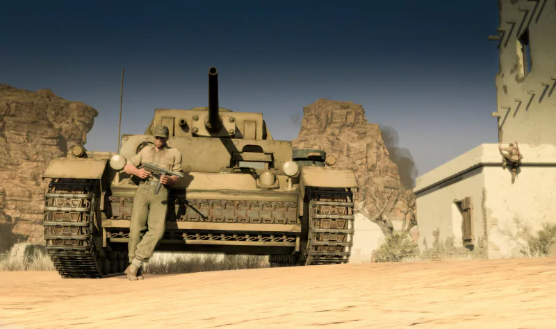 A soldier leans against a large tank in a desert setting from the video game Sniper Elite III, with rocky cliffs and a building in the background.