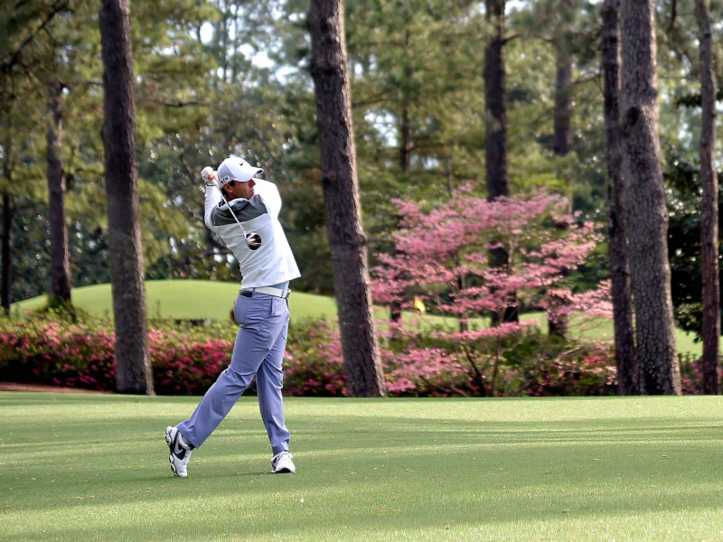 A golfer prepares to swing on a golf course. The image is related to sports and features Rory McIlroy.