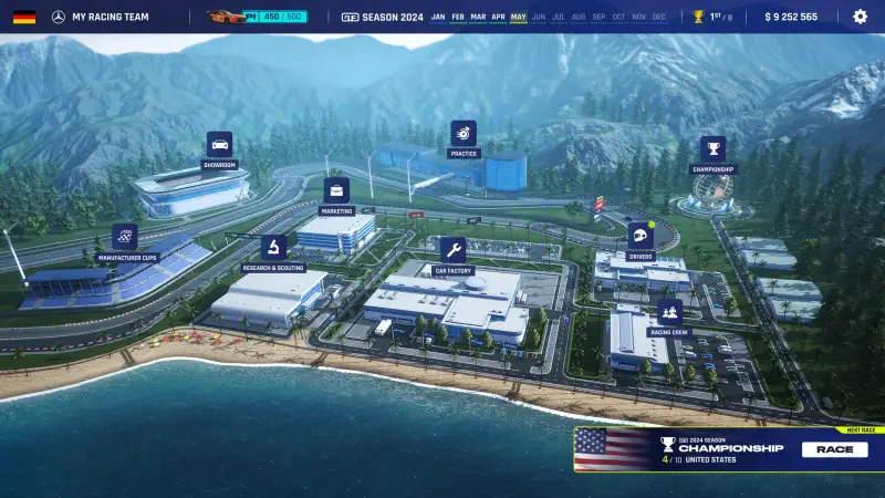 A vibrant aerial view of a racetrack environment in GT Manager, showcasing various team facilities and scenic mountains, with the ocean visible in the foreground.