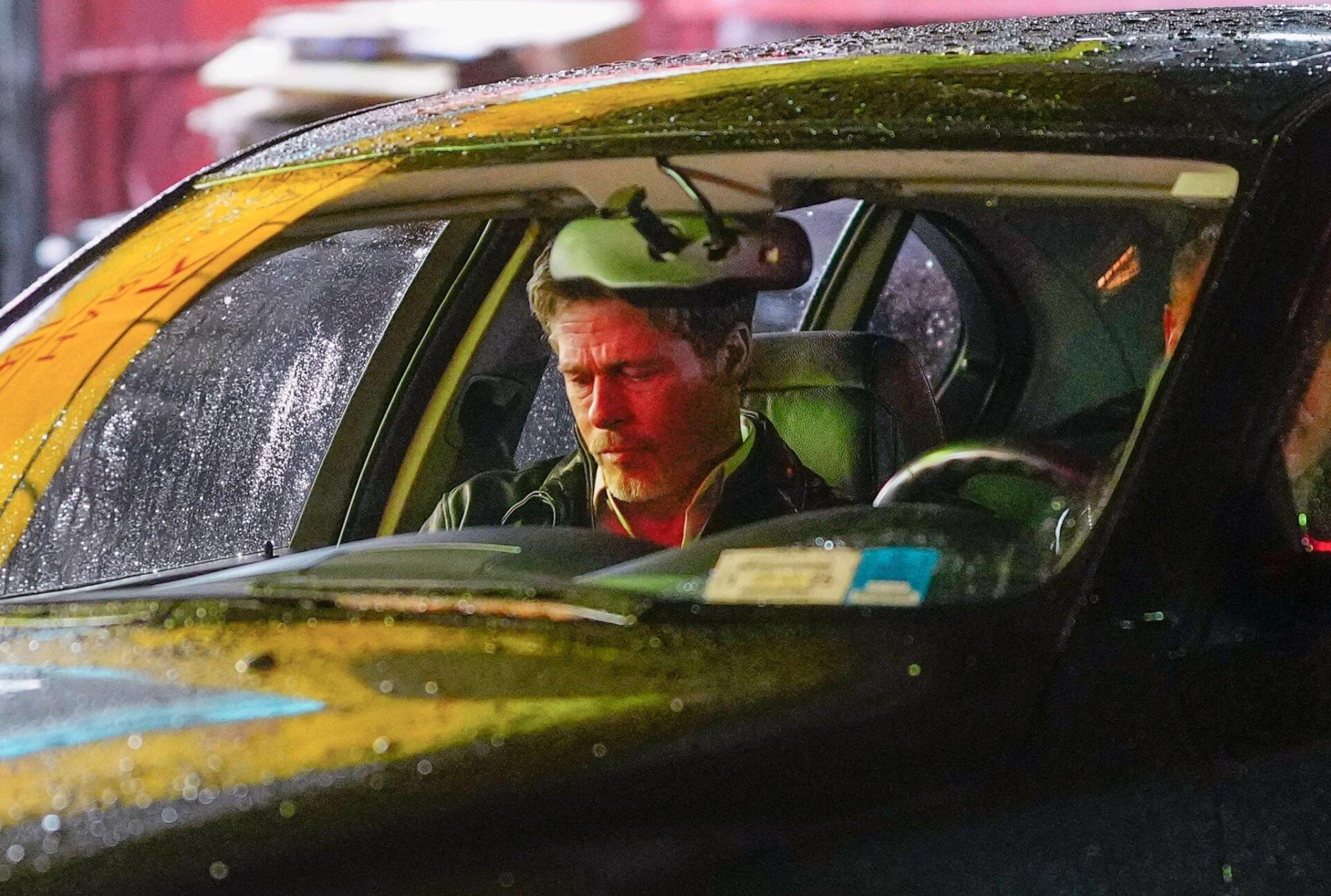 Brad Pitt is seated in a car, looking contemplative amid raindrops on the windshield, in a scene from the 2024 movie Wolfs.