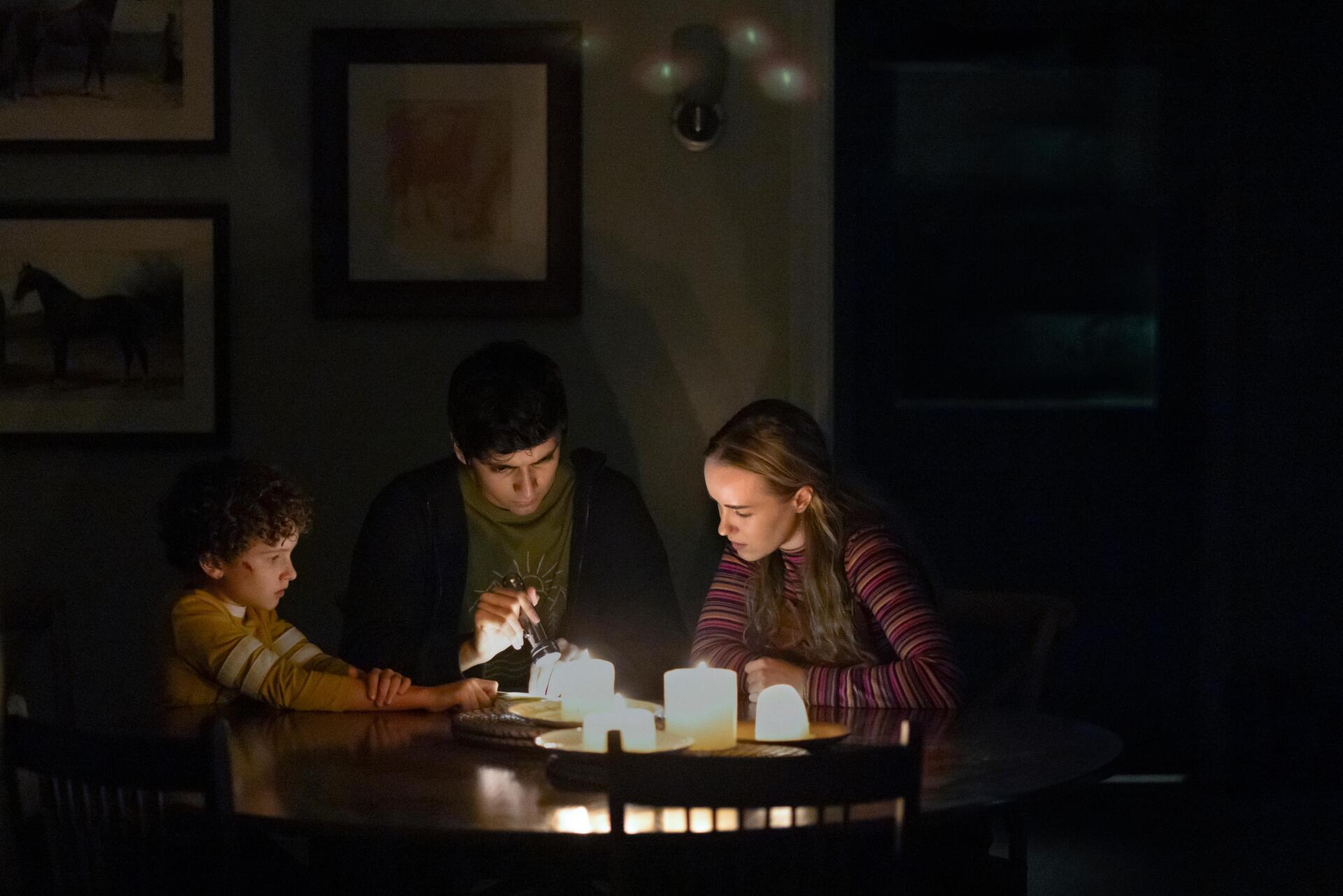A dimly lit room shows three people gathered around a table, engaged in a candlelit activity, capturing a cozy moment from the TV show Teacup (2024).