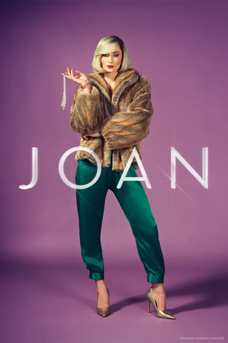Sophie Turner poses confidently in a stylish fur coat and emerald green pants for the TV show Joan, with the title prominently displayed in bold letters beneath her.