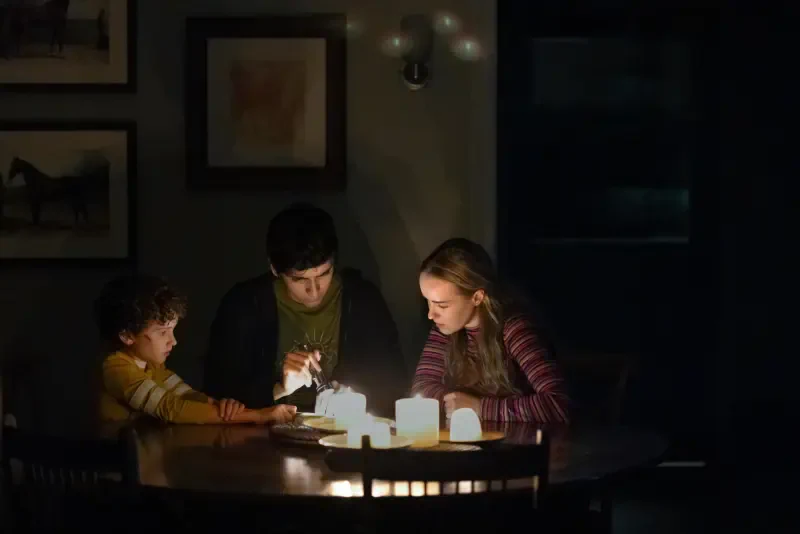 A dimly lit room shows three people gathered around a table, engaged in a candlelit activity, capturing a cozy moment from the TV show Teacup (2024).