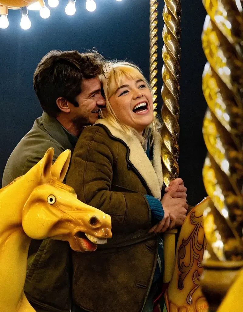 A joyful couple embraces on a carousel in a vibrant scene from the movie We Live in Time, showcasing their connection amid playful surroundings.