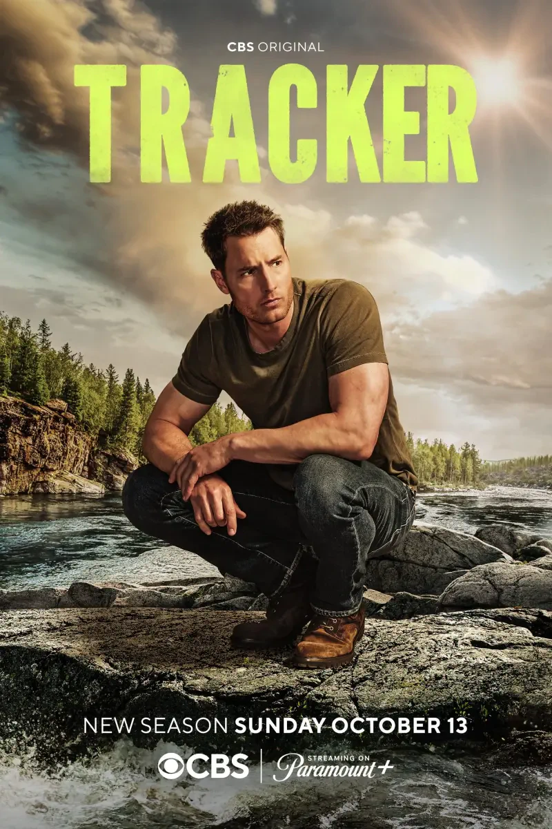 Justin Hartley stars in CBS's Tracker (2024), with the new season launching on October 13. He is featured in a rugged outdoor setting, poised and focused by the water.