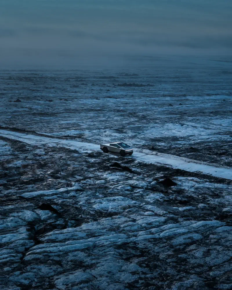 A Tesla Cybertruck navigates a rugged, icy landscape, showcasing its unique design against the stark and dramatic terrain.