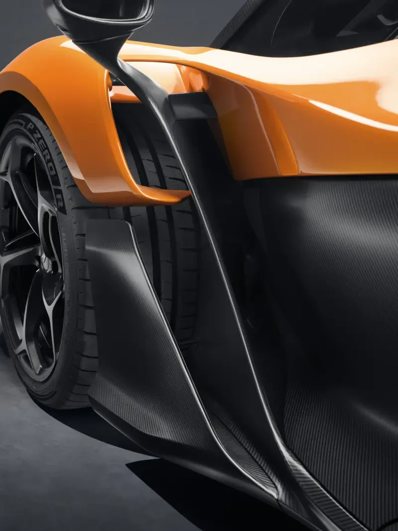 Close-up of a McLaren W1 showcasing its sleek design, featuring bold orange accents and an impressive aerodynamic profile with a detailed side view of the tire and bodywork.