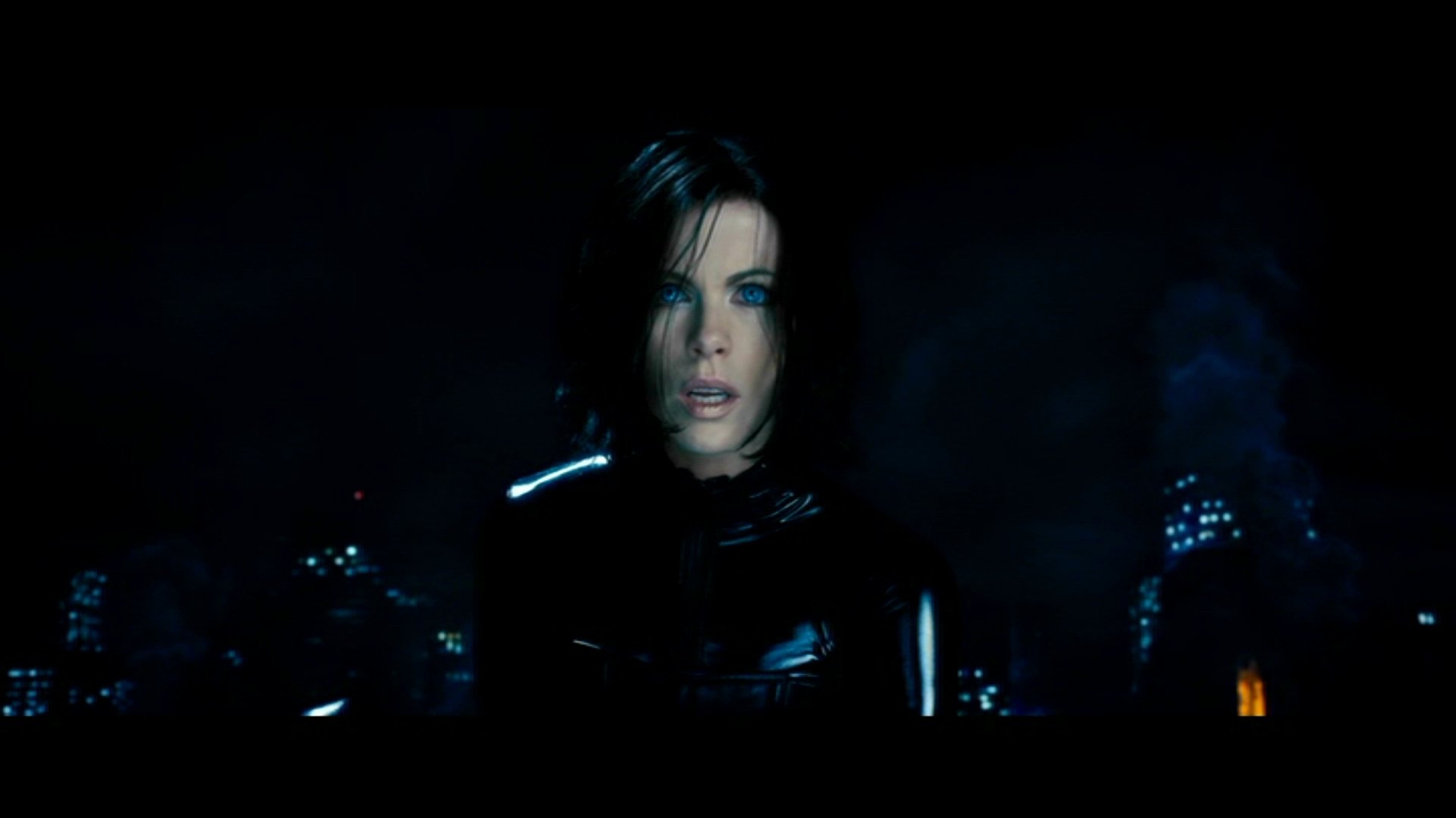 Selene, clad in black leather, stands against a dark, smoky cityscape in a scene from the movie Underworld: Evolution.