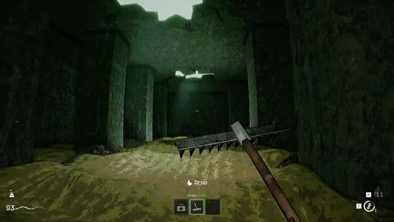 A dark, atmospheric setting in the video game KLETKA, showcasing a shadowy underground environment with columns and a sandy floor, illuminated by a faint light above.