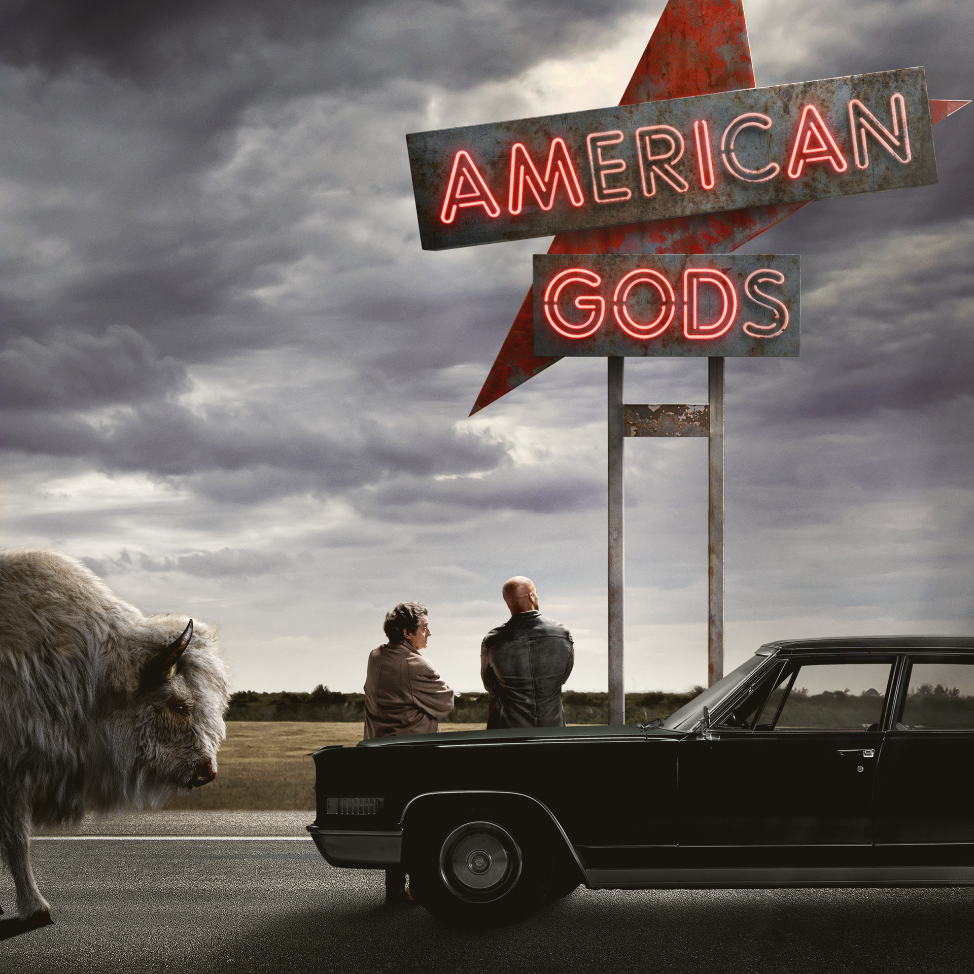 American Gods, TV show: two men sit on a car by a roadside under a neon AMERICAN GODS sign, a large wolf nearby and a stormy sky.