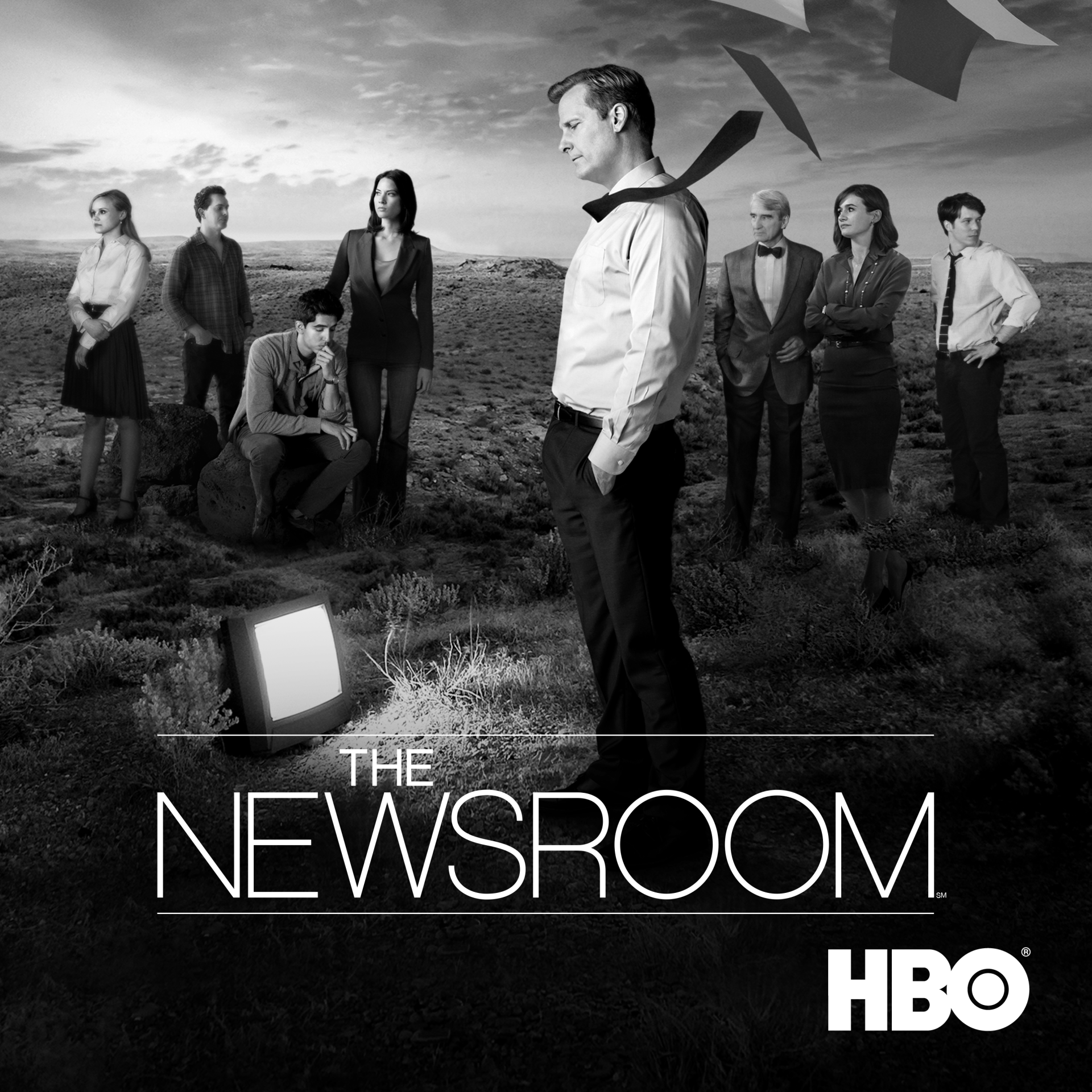 The Newsroom (2012) TV show promo: a news team stands in a windswept field around a discarded TV, papers flying overhead, with the HBO logo visible.