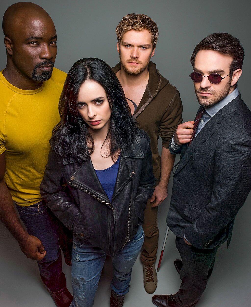Promotional portrait of the four vigilantes from the TV show The Defenders: a suited, sunglass-wearing lawyer; a leather-jacket private investigator; a focused martial artist; and a powerful man in yellow.