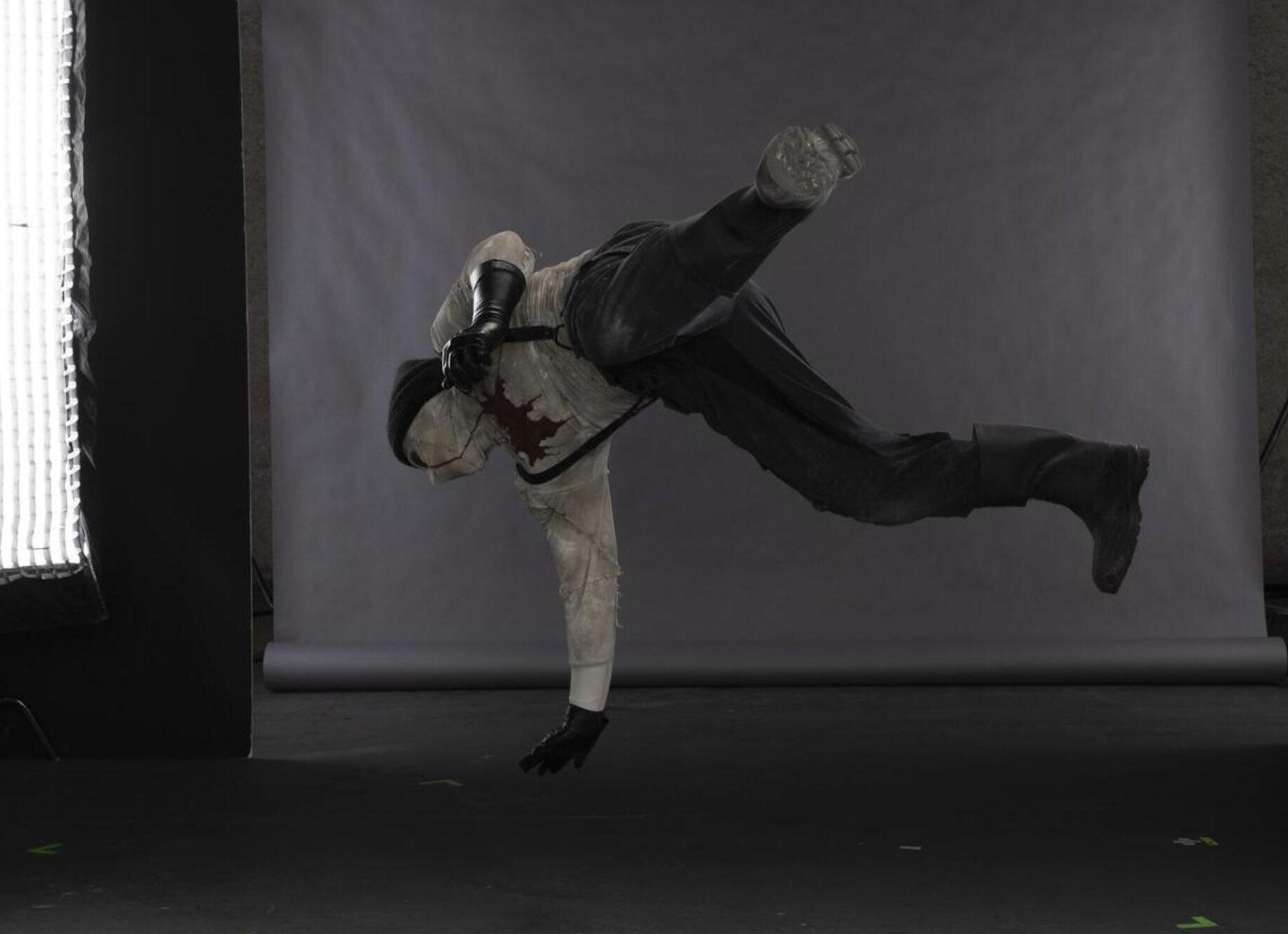 Performer in Daredevil: Born Again (TV show) costume captured mid-air doing a one-handed flip against a gray studio backdrop.