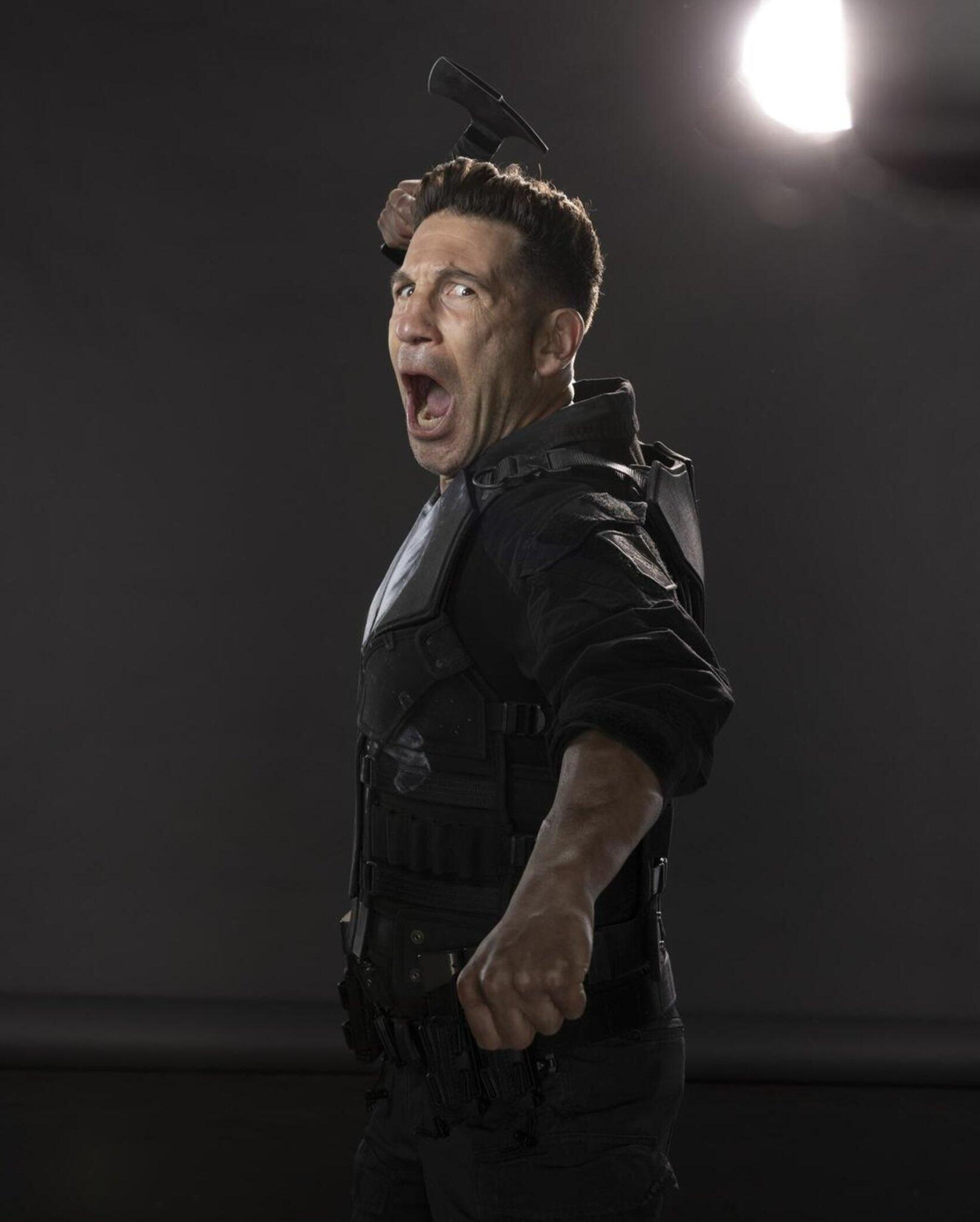 Actor in a tactical suit mid-swing, mouth open as he yells, raised baton and dramatic studio light behind him — promotional image for the TV show Daredevil: Born Again.