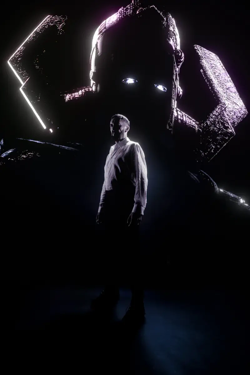 A man stands in shadow before a towering, glowing-eyed figure, evoking a mysterious and powerful scene from The Fantastic Four: First Steps.