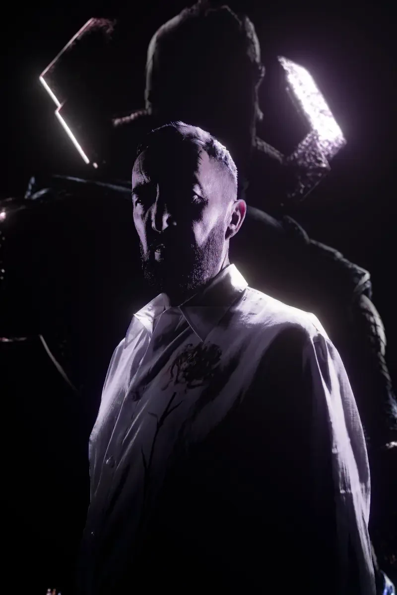 A dramatic, shadowed portrait from The Fantastic Four: First Steps, featuring a man in a stained white shirt with a mysterious figure looming behind him.