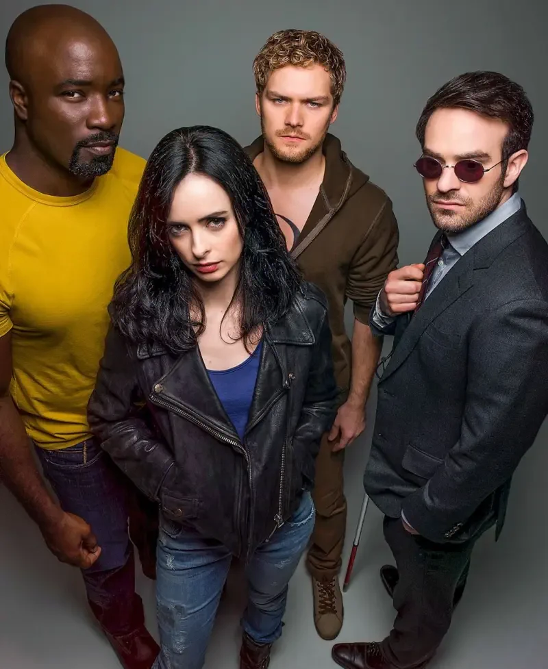Promotional portrait of the four vigilantes from the TV show The Defenders: a suited, sunglass-wearing lawyer; a leather-jacket private investigator; a focused martial artist; and a powerful man in yellow.