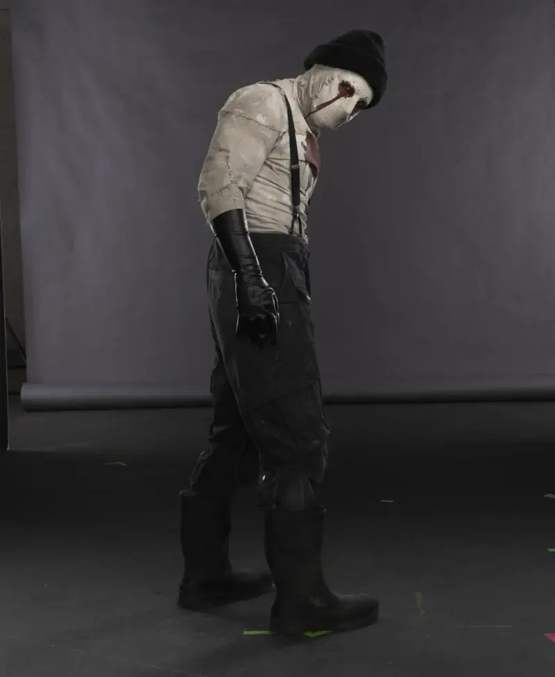 Bandaged, masked figure in suspenders, black gloves and boots walks across a gray studio set — promotional image for the TV show Daredevil: Born Again.