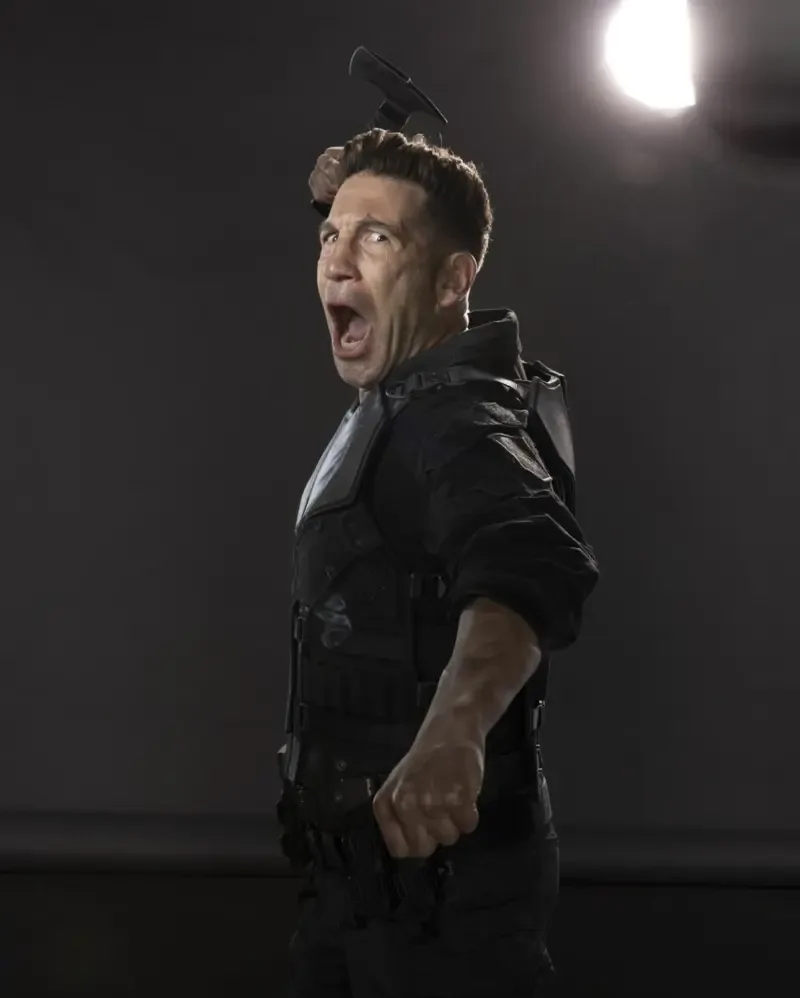 Actor in a tactical suit mid-swing, mouth open as he yells, raised baton and dramatic studio light behind him — promotional image for the TV show Daredevil: Born Again.