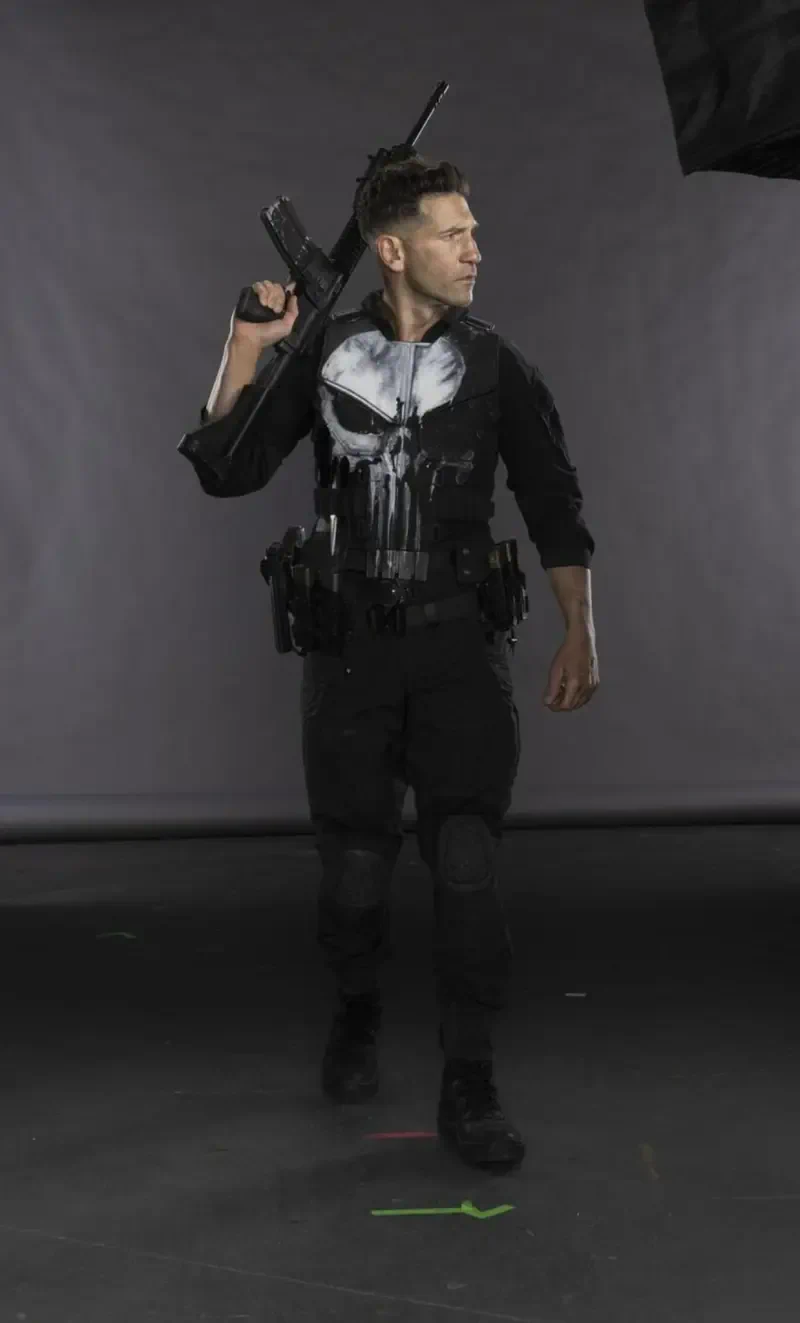 Figure in tactical black gear with a white Punisher skull and rifle walking on a studio set for Daredevil: Born Again (TV show).
