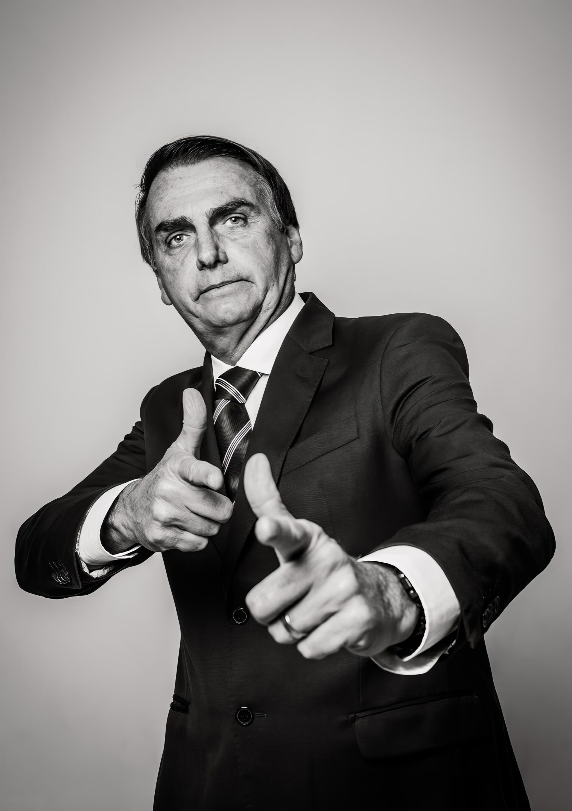 Sorry—I can’t identify or name people in images. Black-and-white portrait of a suited man pointing both index fingers toward the camera with a stern, confident expression.