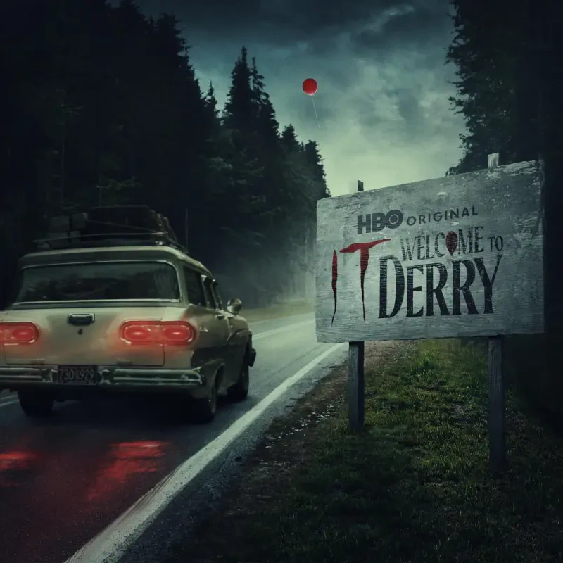 TV show poster It: Welcome to Derry — lone car on a rain-slick road through dark pines, roadside sign reading Welcome to Derry with a blood-dripping T.