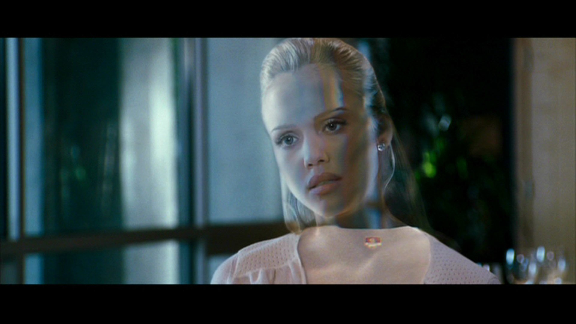 Close-up of a translucent woman from the movie Fantastic Four, her reflection layered over her face as she gazes pensively inside a dim room.