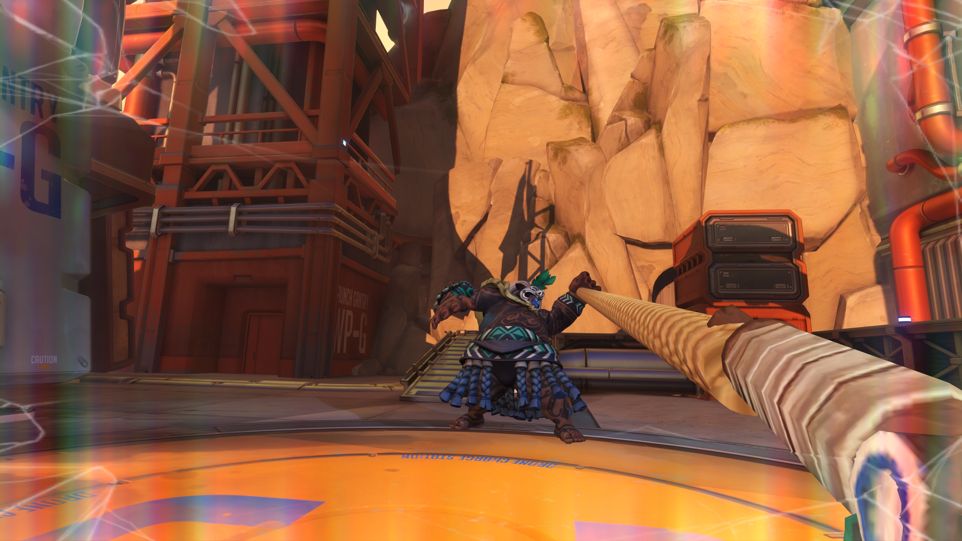 Roadhog from the video game Overwatch launches his chain hook toward the camera across a rocky industrial map, seen from the perspective of the hooked character.
