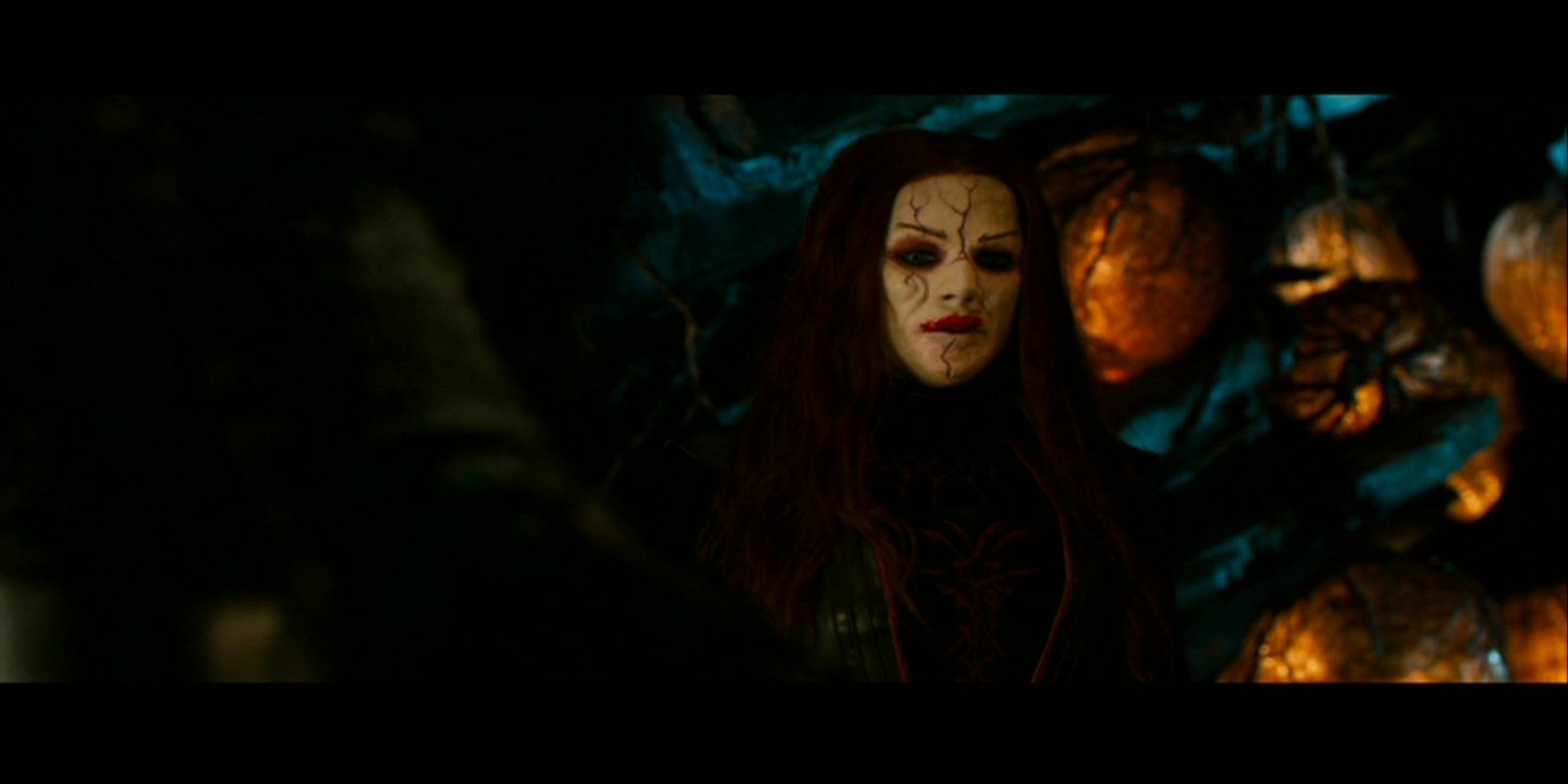 Dark, eerie still from Hansel & Gretel: Witch Hunters — a pale, scarred witch with long red hair stands amid glowing, pumpkin‑like lanterns in a shadowy forest.
