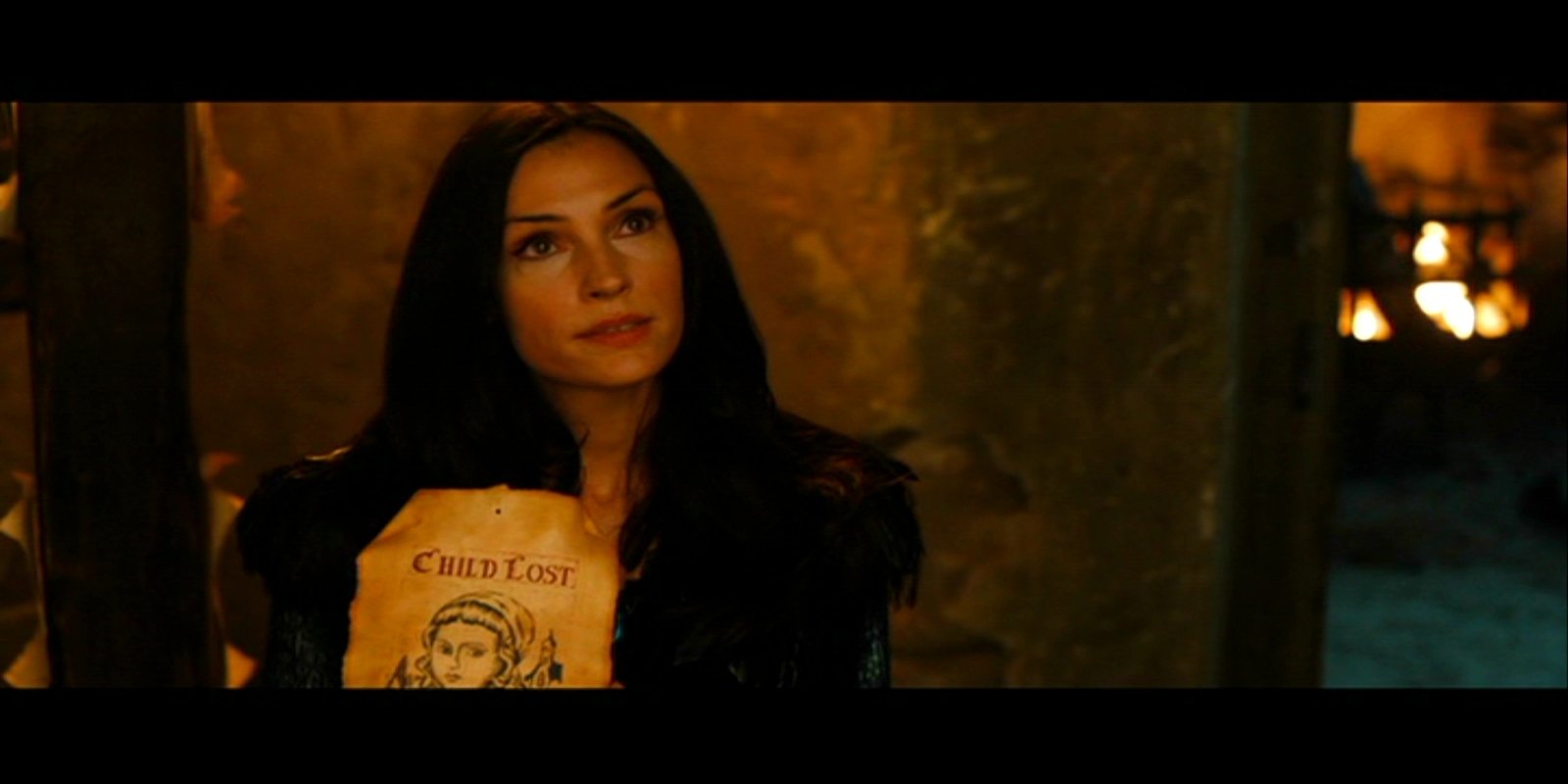Hansel & Gretel: Witch Hunters still — dark-haired woman holds an illustrated children's book in a dim, firelit interior.