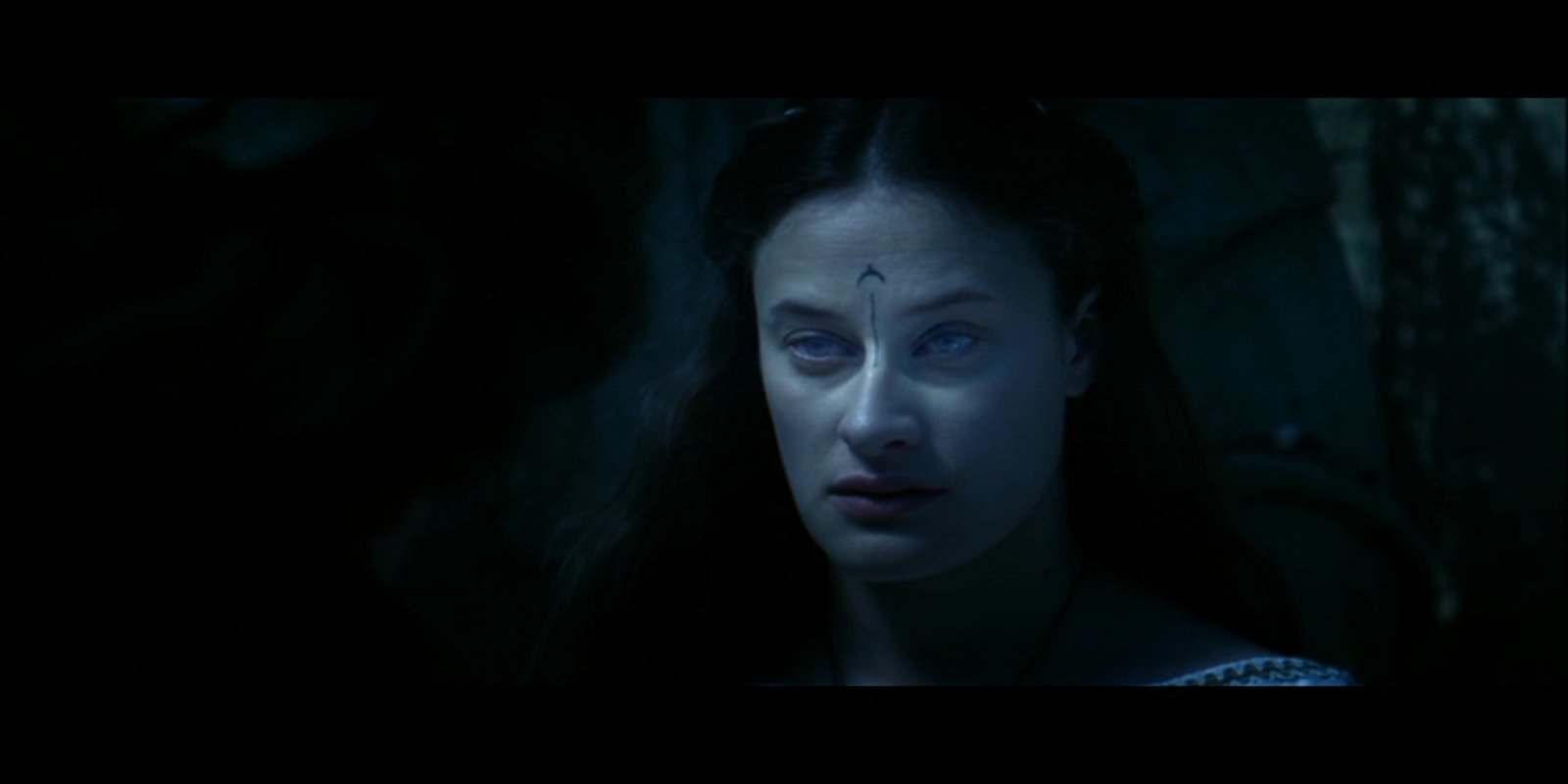 Close-up of a pale, dark-haired woman with a small forehead mark, bathed in blue shadow in a forest scene from the movie The Legend of Hercules.